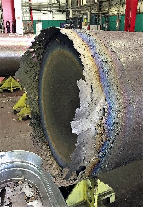 Photograph of the end of a titanium ingot with a rough, flaking surface and heavy crown material around the rim.