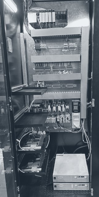 Photograph of an open control cabinet with a PLC rack at the top, terminal rows, a drive, driver boards and two power supplies at the bottom.