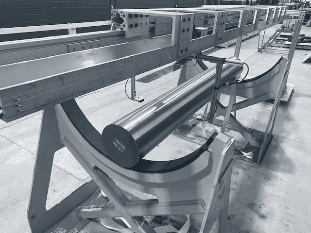 Photograph of an aluminum extrusion rail with a sensor carriage above a round billet resting on yellow cradles.