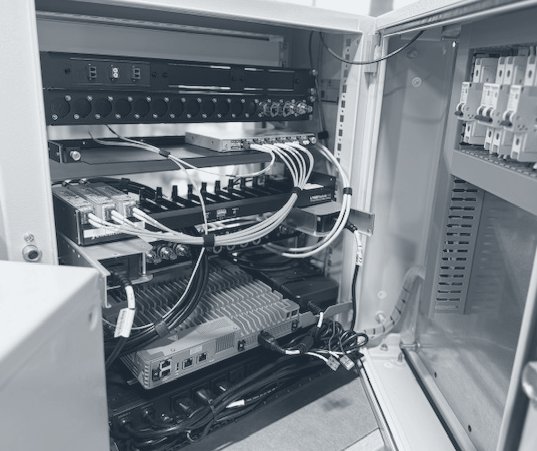 Photograph of an open control-room cabinet with a fiber patch panel, an SDI distribution unit, a recorder, a switch and breakers.