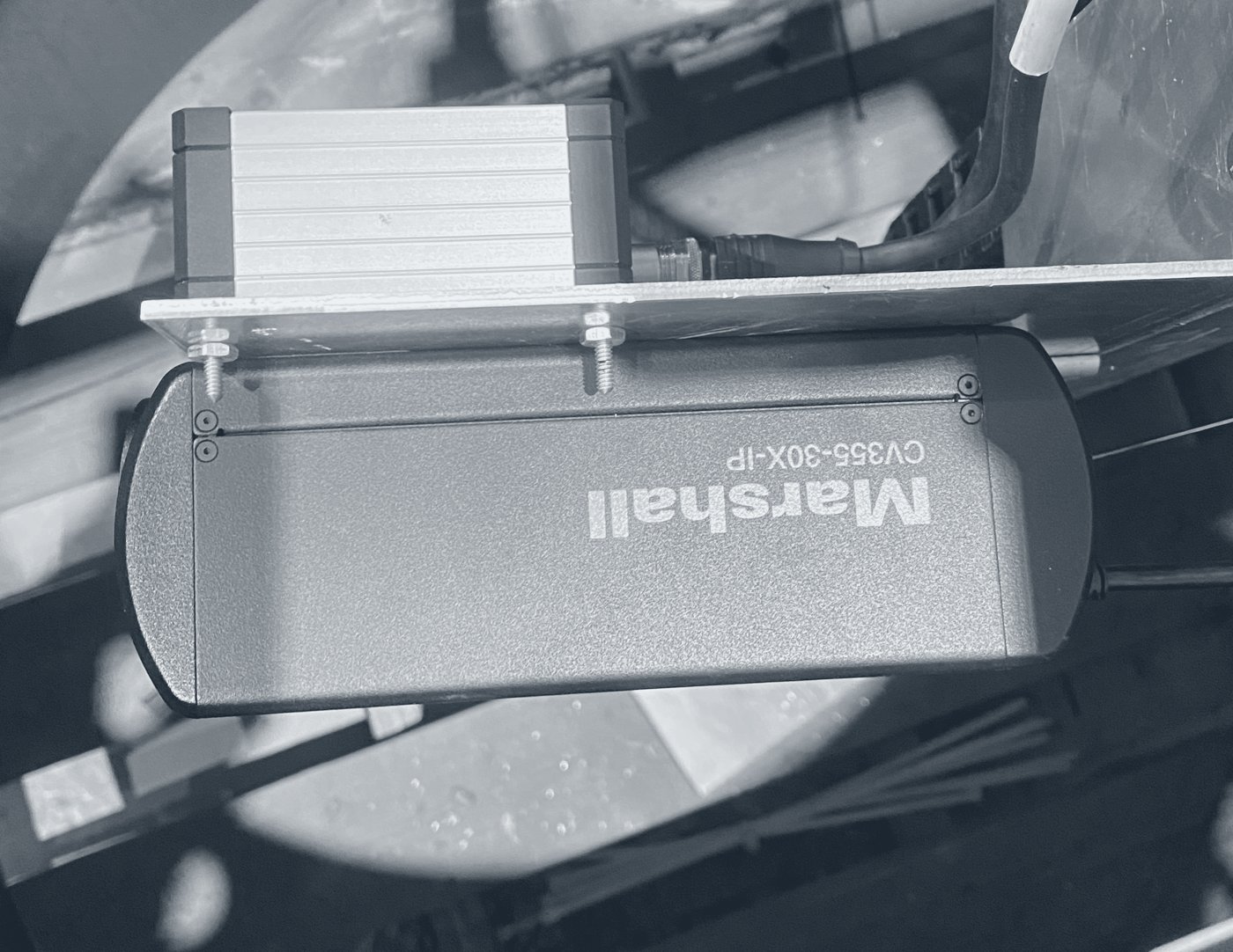 Photograph looking into a camera housing: a compact camera on a bracket, with its cable, behind a round viewport.